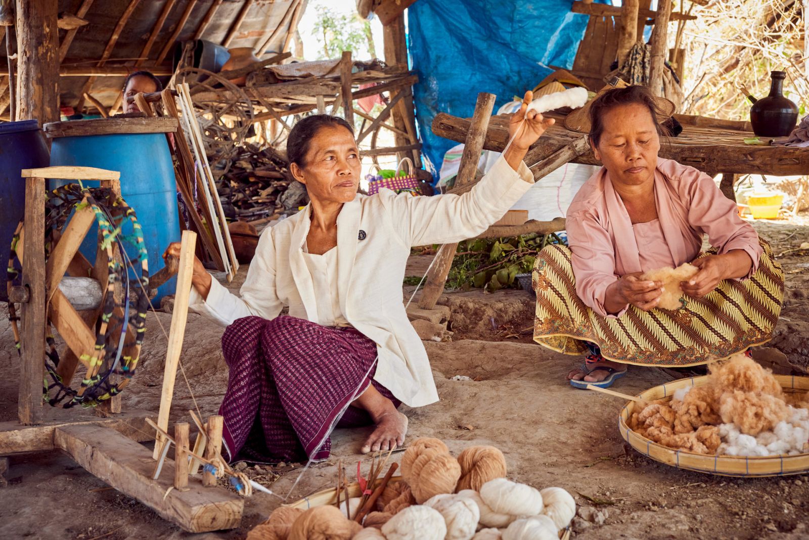 SukkhaCittaâs Ibu Kasmini, an Indonesian farmer who has inherited her farming practices from her grandmother, using a spinning wheel to turn cotton into threads while Ibu Karmini prepares the cotton behind her.