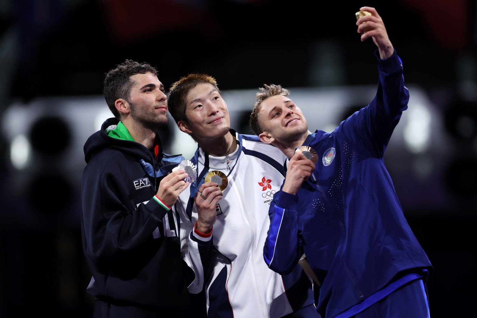 PARIS, FRANCE - JULY 29: Ka Long Cheung of team Hong Kong  (C), Silver medalist Filippo Macchi of team Italy (L) and Bronze medalist Nick Itkin of United States(R) take a selfie on the podium during the Men's Foil Individual medal ceremony on day three of the Olympic Games Paris 2024 at Grand Palais on July 29, 2024 in Paris, France. (Photo by Carl Recine/Getty Images)